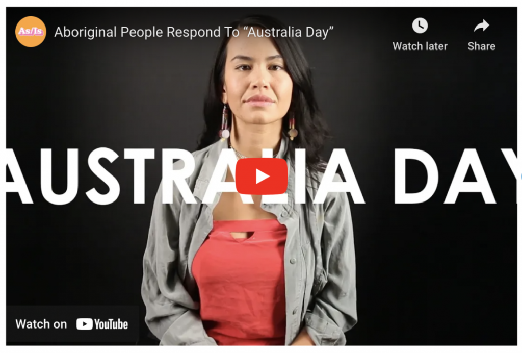 Video screenshot: Aboriginal People Respond to "Australia Day" with image of an aboriginal person with long hair and dangly earrings, wearing an orange top with long sleeve gray button up shirt over.