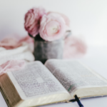 A bible open with short vase of pink flowers.