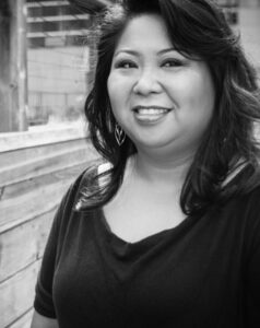 Dawn Mabalon smiles with a wood and wire fence behind her.