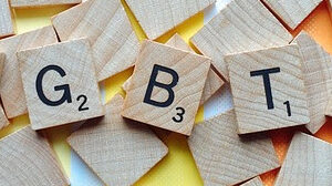 Scrabble tiles spelling out LGBTQ with pastel rainbow pattern in the background.