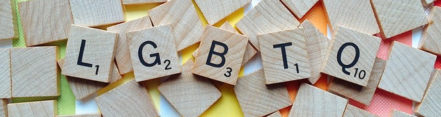 Scrabble tiles spelling out LGBTQ with pastel rainbow pattern in the background.