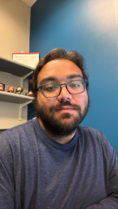 Anthony Rodriguez wearing a dark shirt in his office, with shelves and funko pop statues in the background.