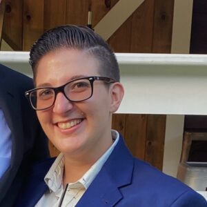 Ellie Beargeon smiles wearing glasses and a blue blazer.