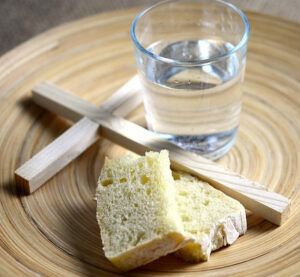 A wooden cross with pieces of bread and a glass of water on a plate.