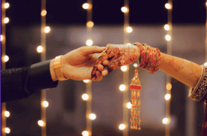 Desi couple holding hands wearing vintage jewelry and henna with lights in the background.