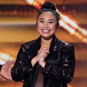 Jessica Sanchez wearing a sparkly jacket and her hair in a bun, a hand on her right elbow.