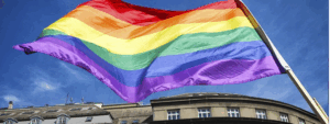 Rainbow flag symbolizing Pride Month with stone buildings below.