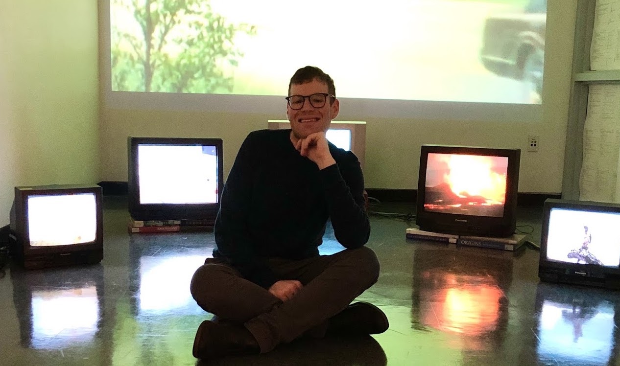 Philip sits cross-legged in the middle of the room, surrounded by old television screens