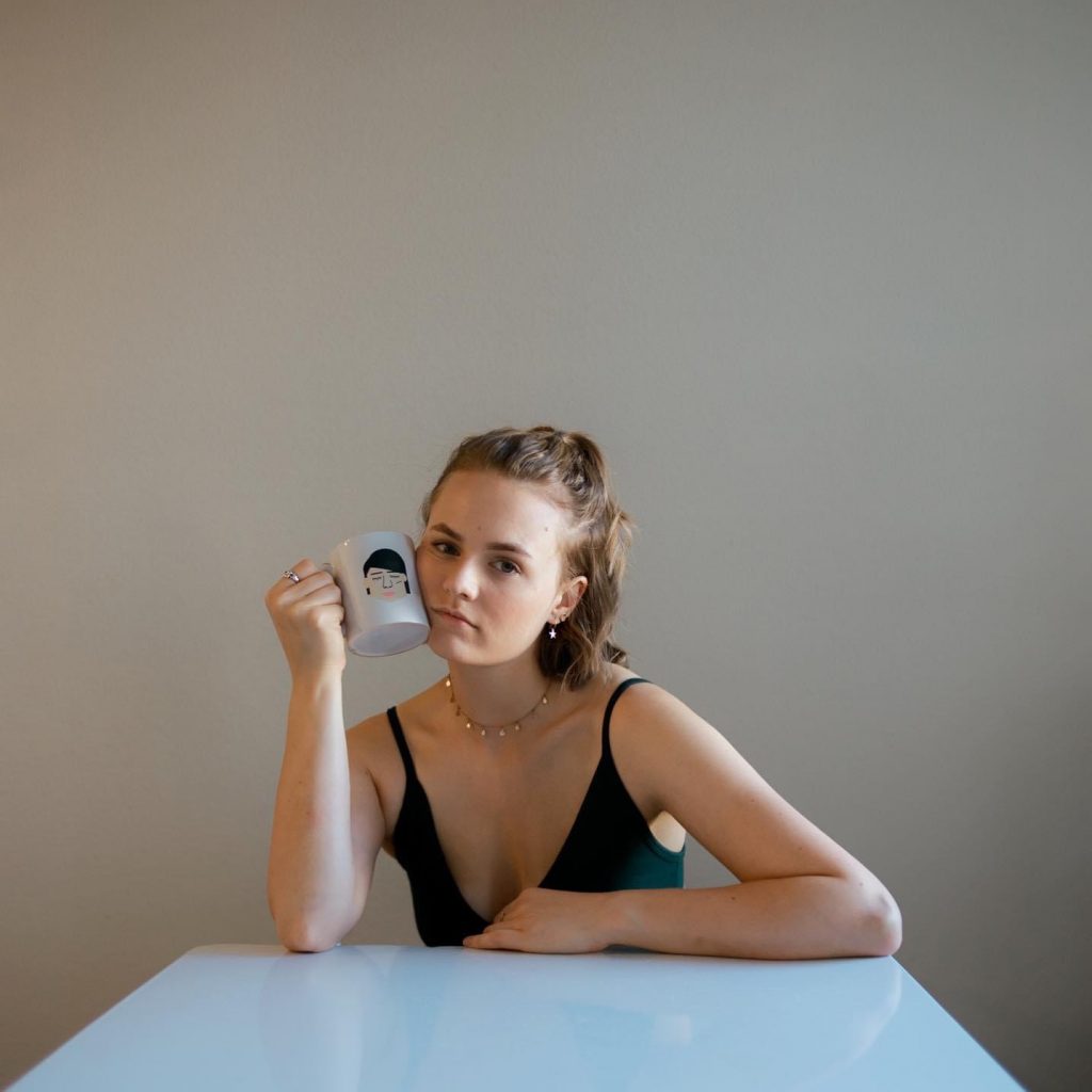 Courtney posing and smiling while holding a mug sitting at a table.