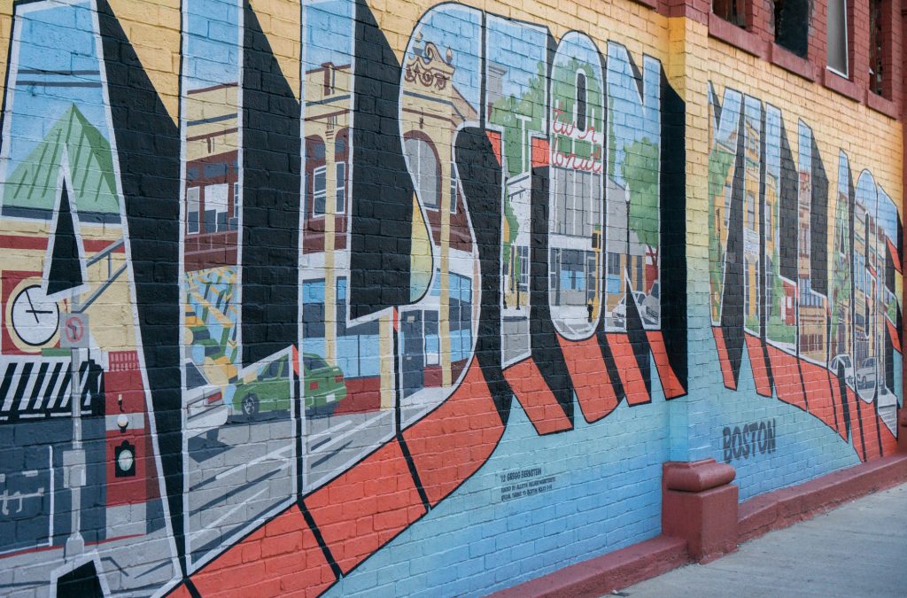A photo of the Greetings From Allston mural, painted on a brick wall