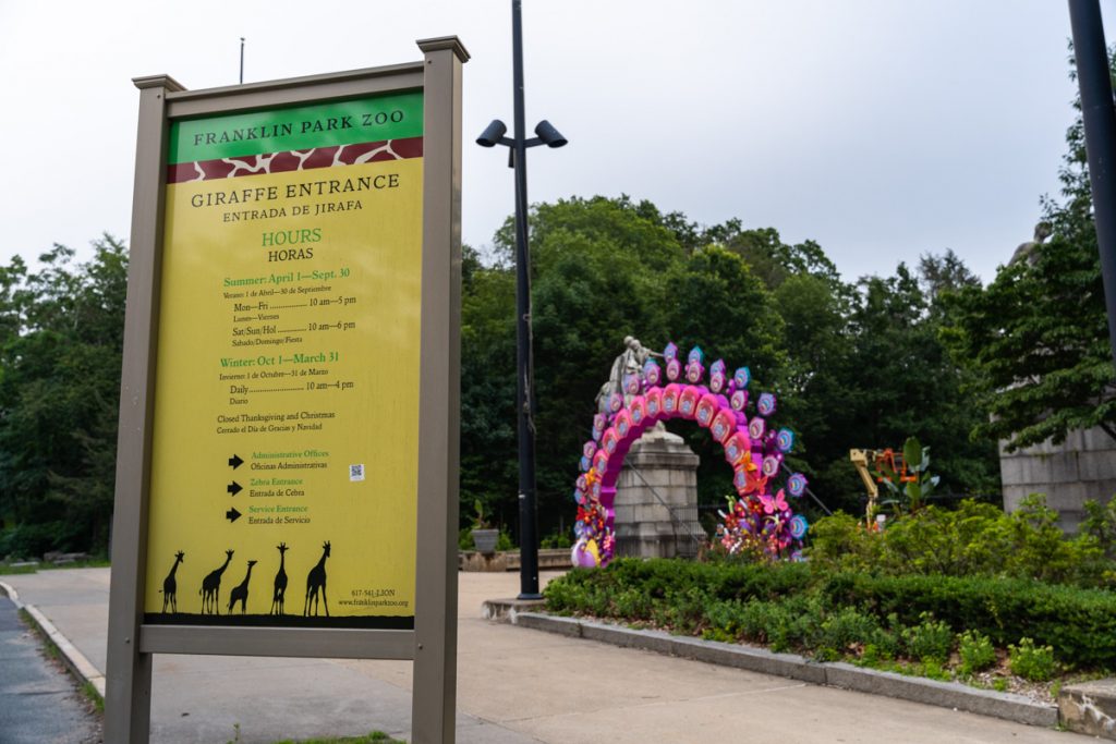 An entrance sign listing the hours to the Franklin Park and Zoo in front of the entryway of the Park.