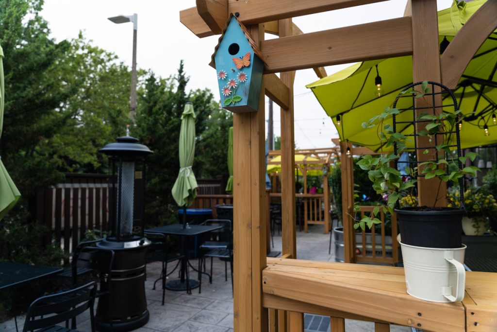 An outdoor patio with dining chairs and umbrellas and a birdhouse. 