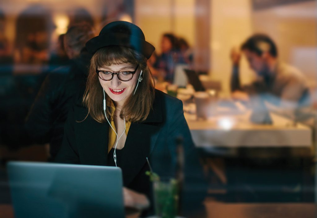 Graduate student smiling while using laptop computer in a cafe.