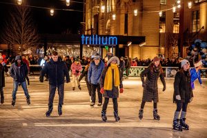 Boston winter ice skaters on the ice at Rink 401 with the Trillium Brewing sign illuminated behind them.