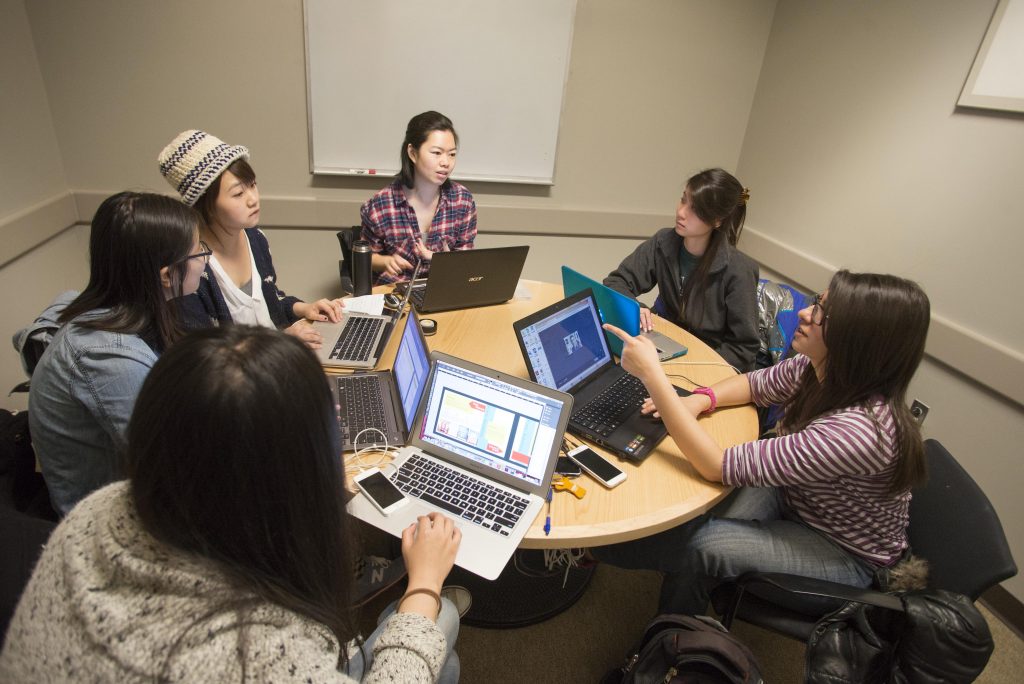A group of students sits at a table with their laptops open while studying together.