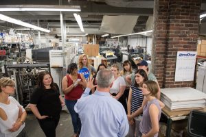 Emerson students gathered around a professional explaining the lithography and printing presses behind them.