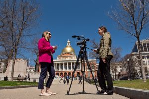 An Emerson student interviews a staffer in front of the State House as part of their internship and coursework.