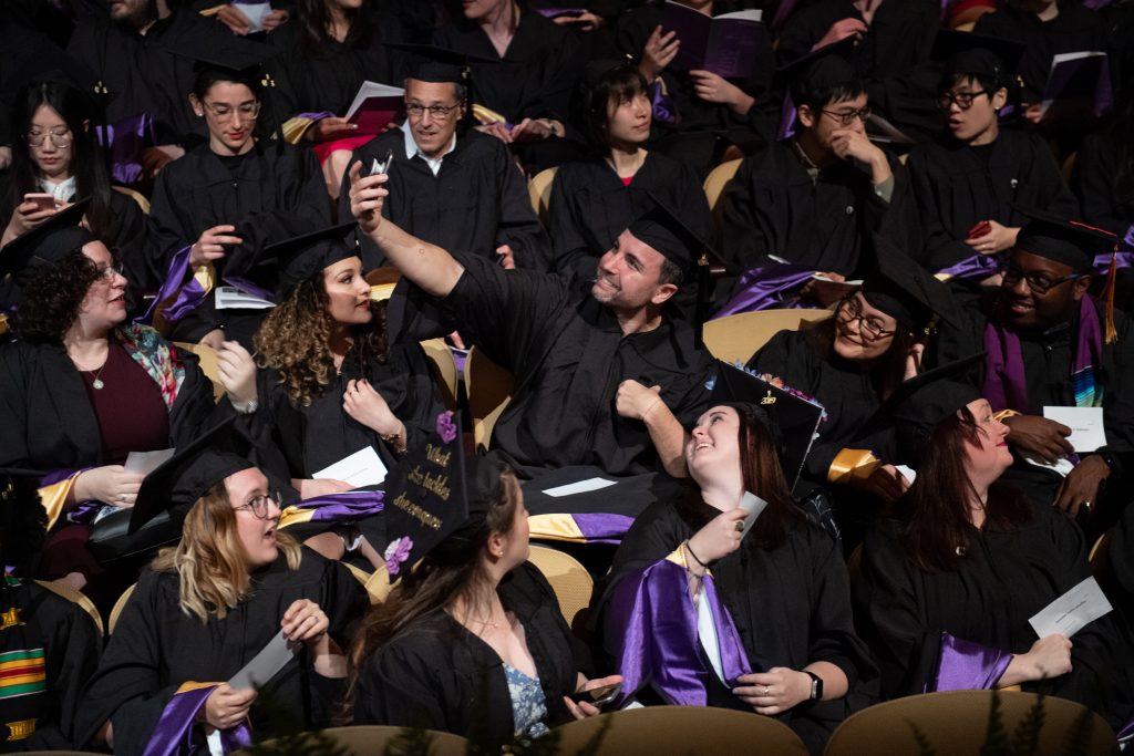 Students smile and take a selfie together during their graduation ceremony.