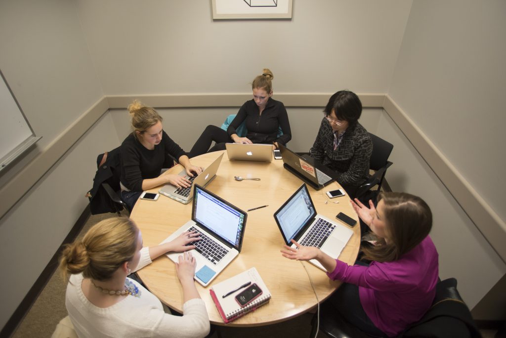 Five students working on laptops in one of the library's private study rooms. 
