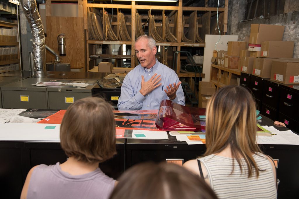 A book publishing/printing professional sitting at a work table with materials in front of him speaks to Emerson students about a career in book printing.