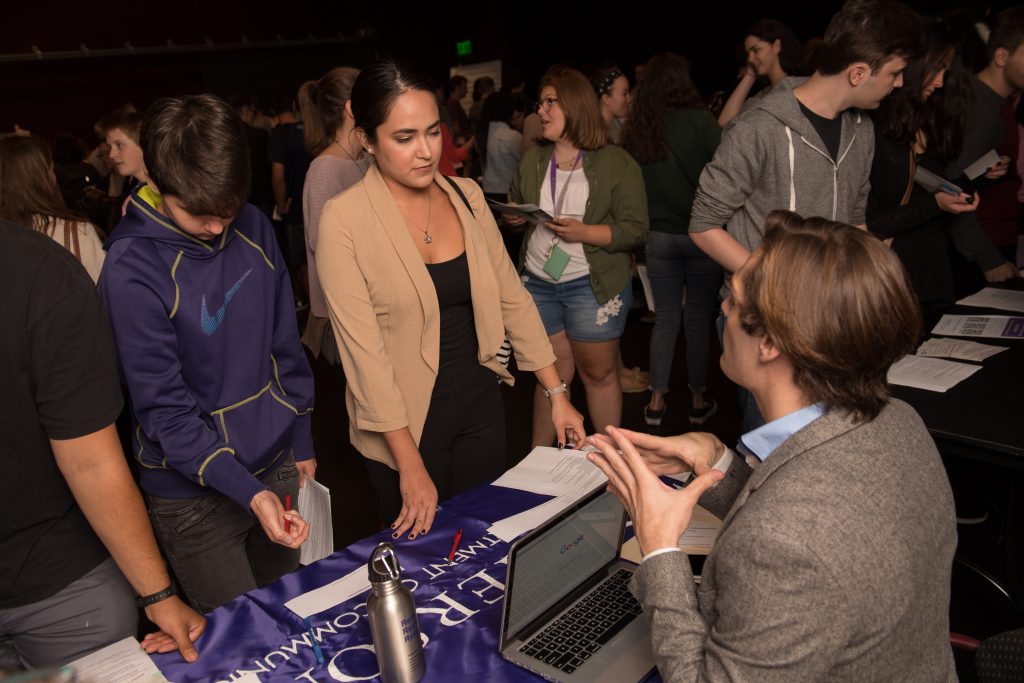 Emerson student at a job fair table, speaking to a career representative.