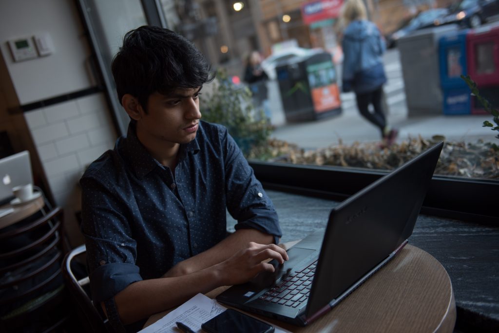 Graduate student working on laptop in cafe, seated near window.