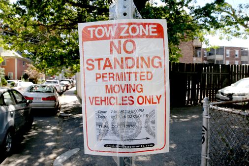 A printed sign reading "Tow Zone - No standing permitted - Moving vehicles only"