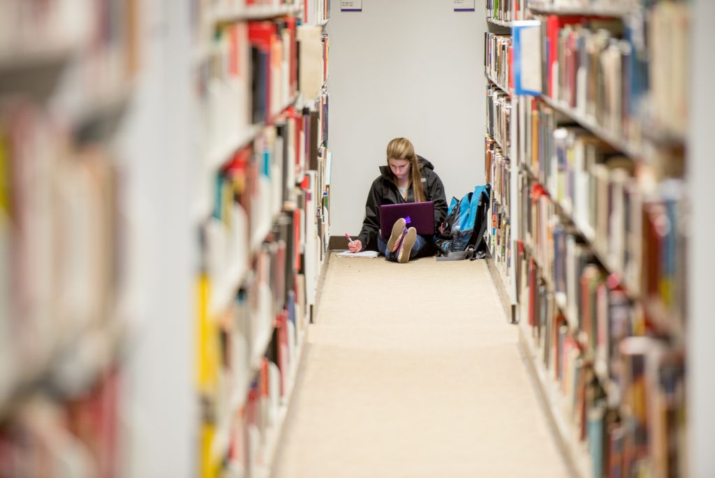Girl sitting on the floor of a library studying