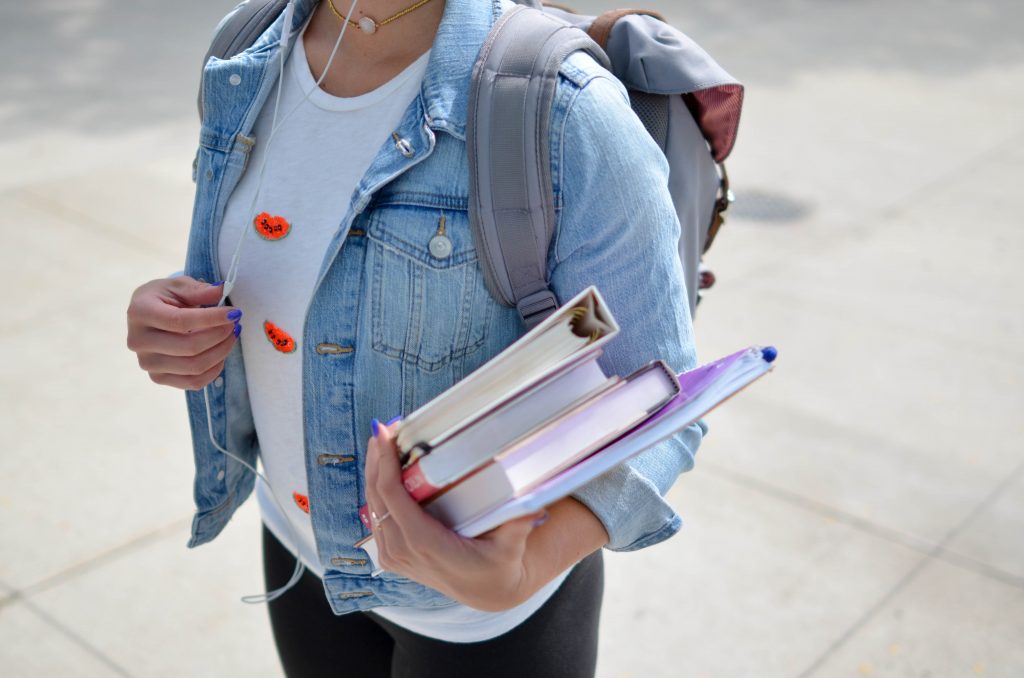 Graduate student walks with textbooks and a backpack
