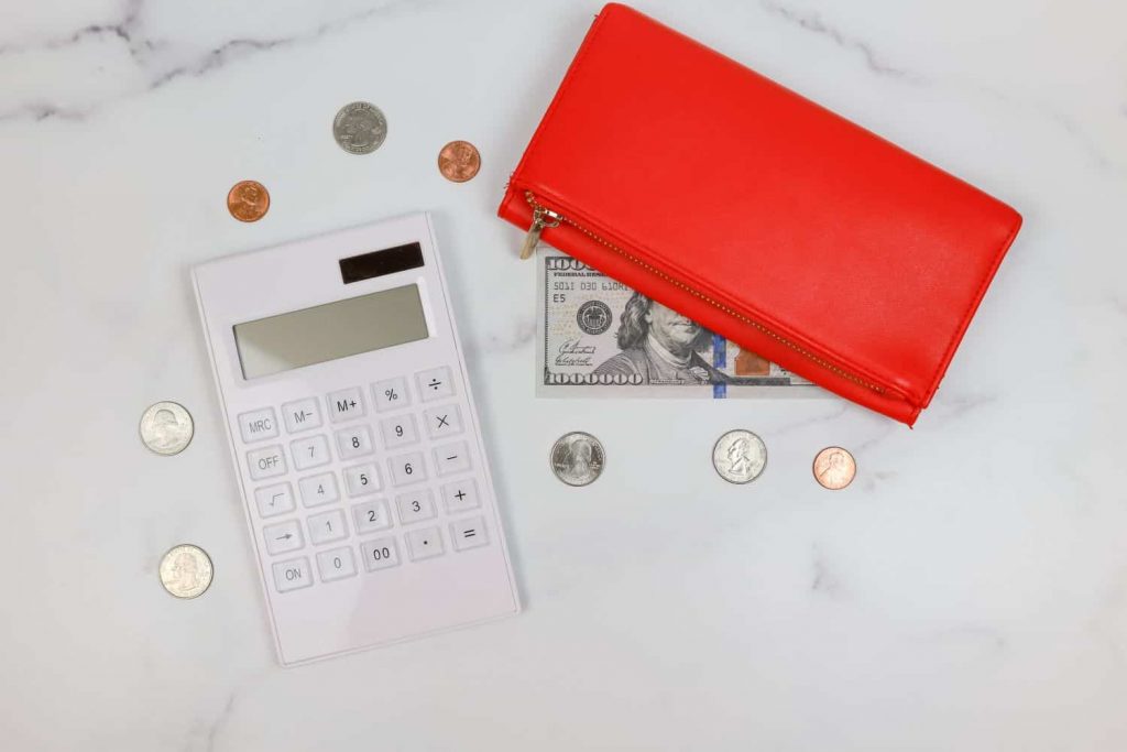 A calculator, various coins, a wallet, and a $100,000 bill on a white countertop.