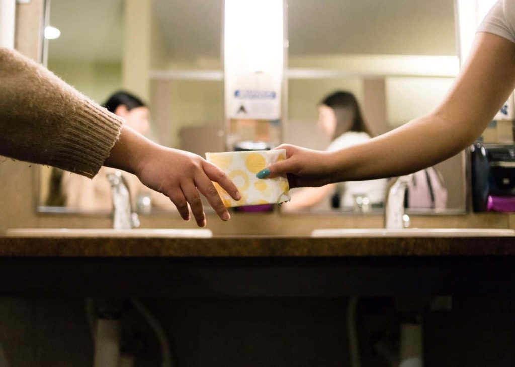 One person offering another person a menstrual pad