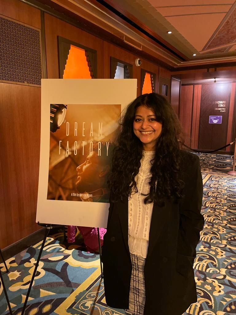 Aarushi Nigam standing in front of the title poster for her film, Dream Factory