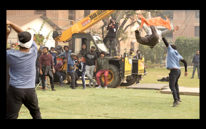 Actors in a Bollywood film shooting a scene outside while below-the-line crew stand and manage equipment
