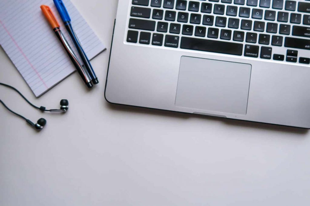 A laptop keyboard, pens, a notepad, and headphones 