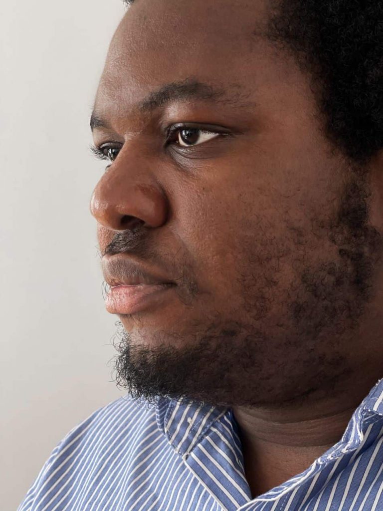 Close-up portrait of Tochukwu Okafor, a current Creative Writing MFA student, wearing a blue and white striped button-down