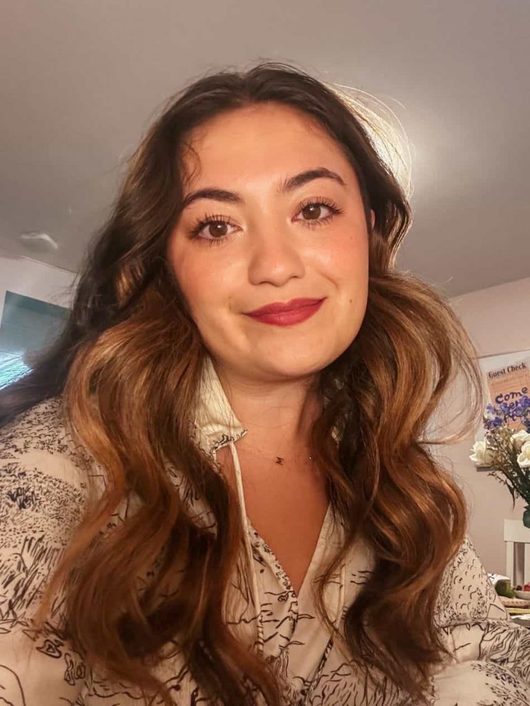 Natalie Rosselli, smiling at the camera in a white blouse with an abstract pattern