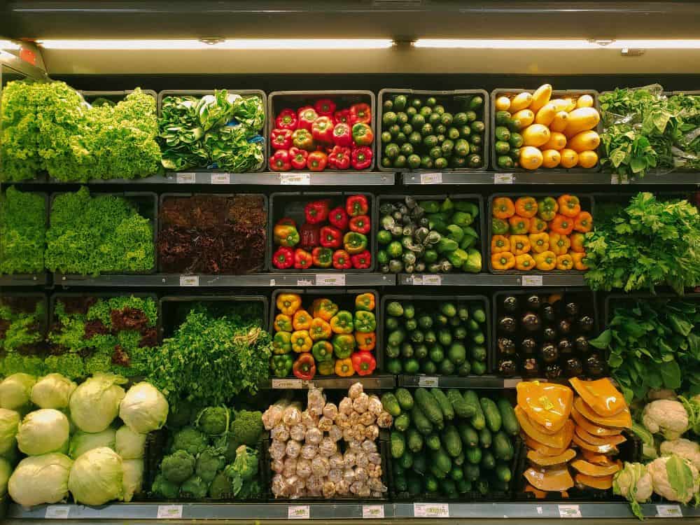 Shelves at a grocery store filled with green, yellow, and red vegerables such as lettuce, peppers, zucchini, melon, and more.