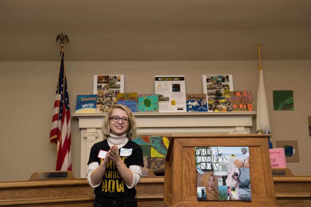 An Emerson student standing in the front of room with a podium and flags, leading a political activism event