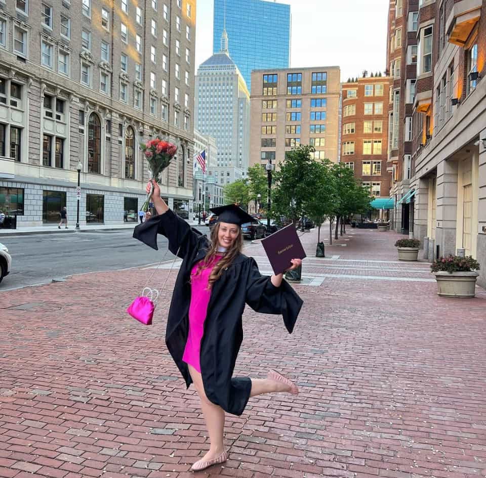 Kate Dubovikova in her cap and gown, posing with flowers and her diploma holder in downtown Boston.