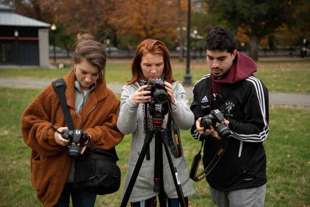 Three Emerson students using professional cameras to photograph the the Boston Common. The middle student holds her camera on a tripod.