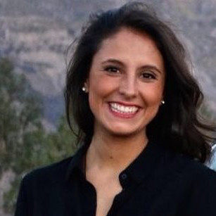Luciana Paz, smiling and standing in front of a hilly background. She has long dark hair and a black blouse.