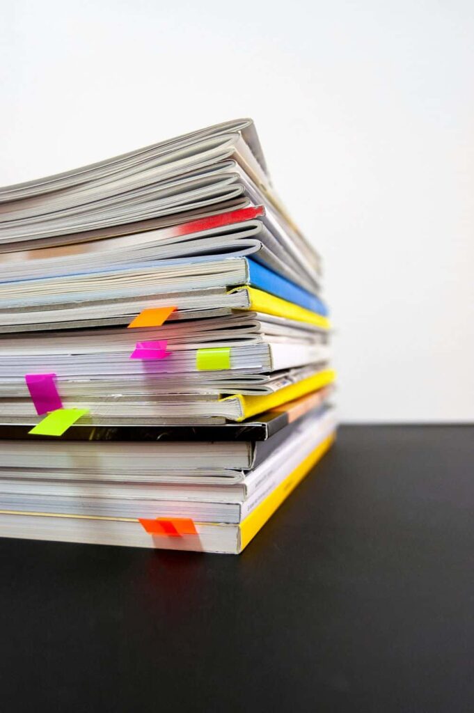 A stack of magazines marked with sticky notes. They sit on a black table