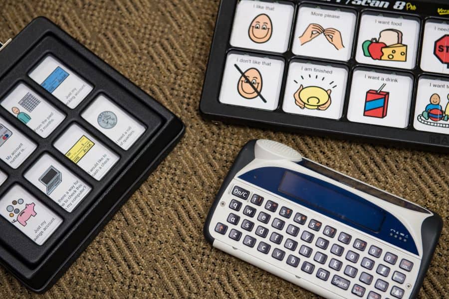 Three different Alternative/Augmentative Communication (AAC) devices. Two AAC devices have a grid of illustrations paired with words that the user can select to indicate their message. The third AAC device is a keyboard to type the user's message.