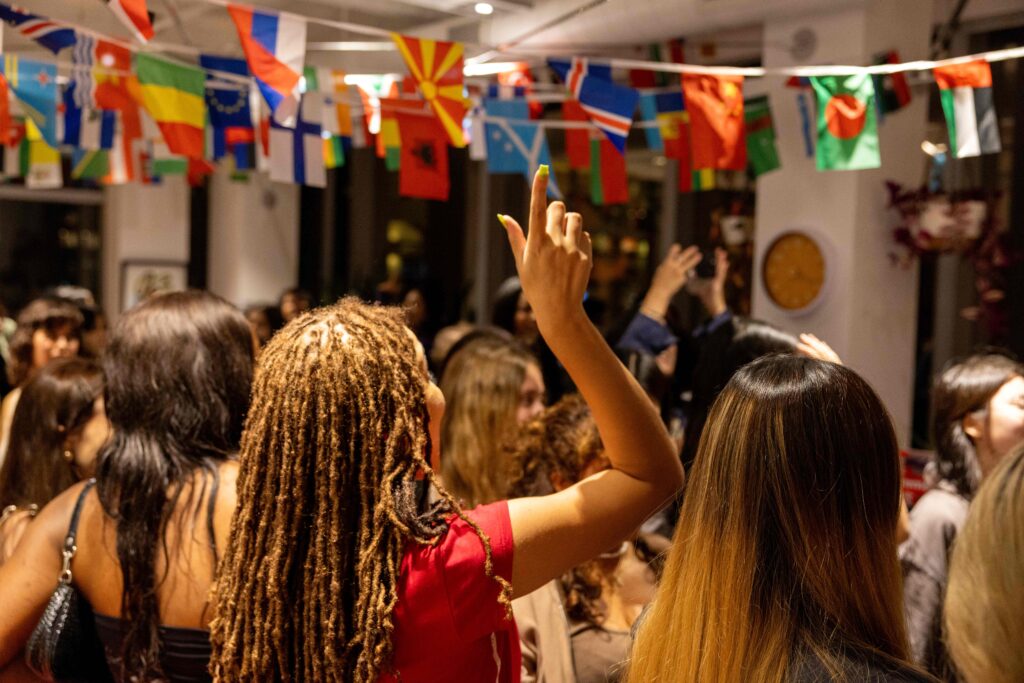 Students enjoying a cultural celebration in a room with various nations' flags hanging from the ceiling.