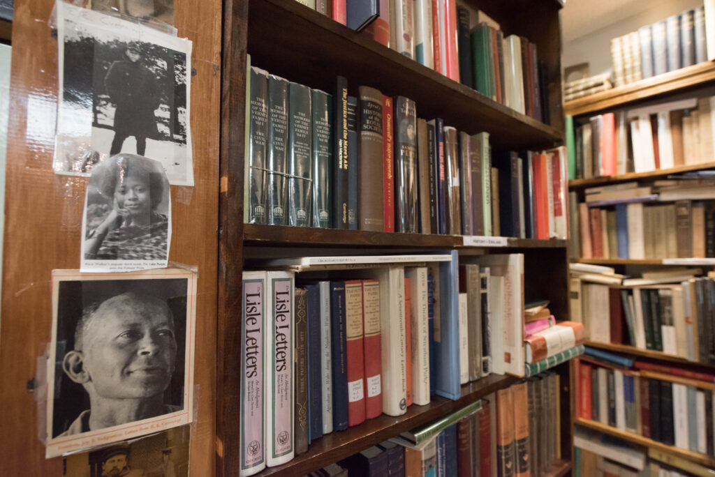 Bookcase in a store with several miscellaneous books and photos of authors in black and white.