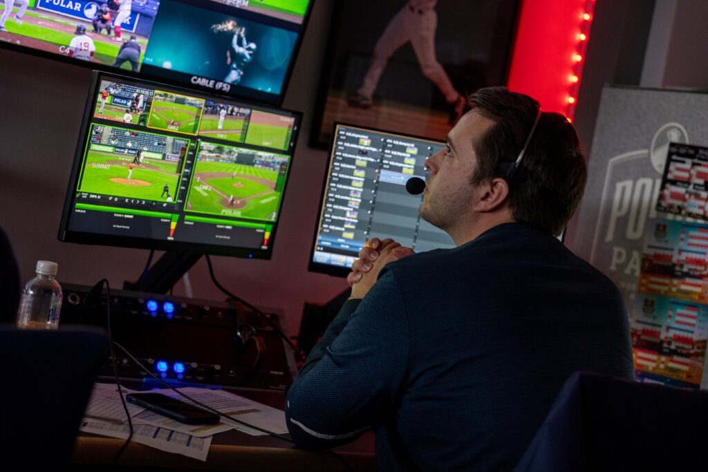 A man sits in front of three monitors as he analyses different baseball plays as part of Emerson's Sports Communication program.