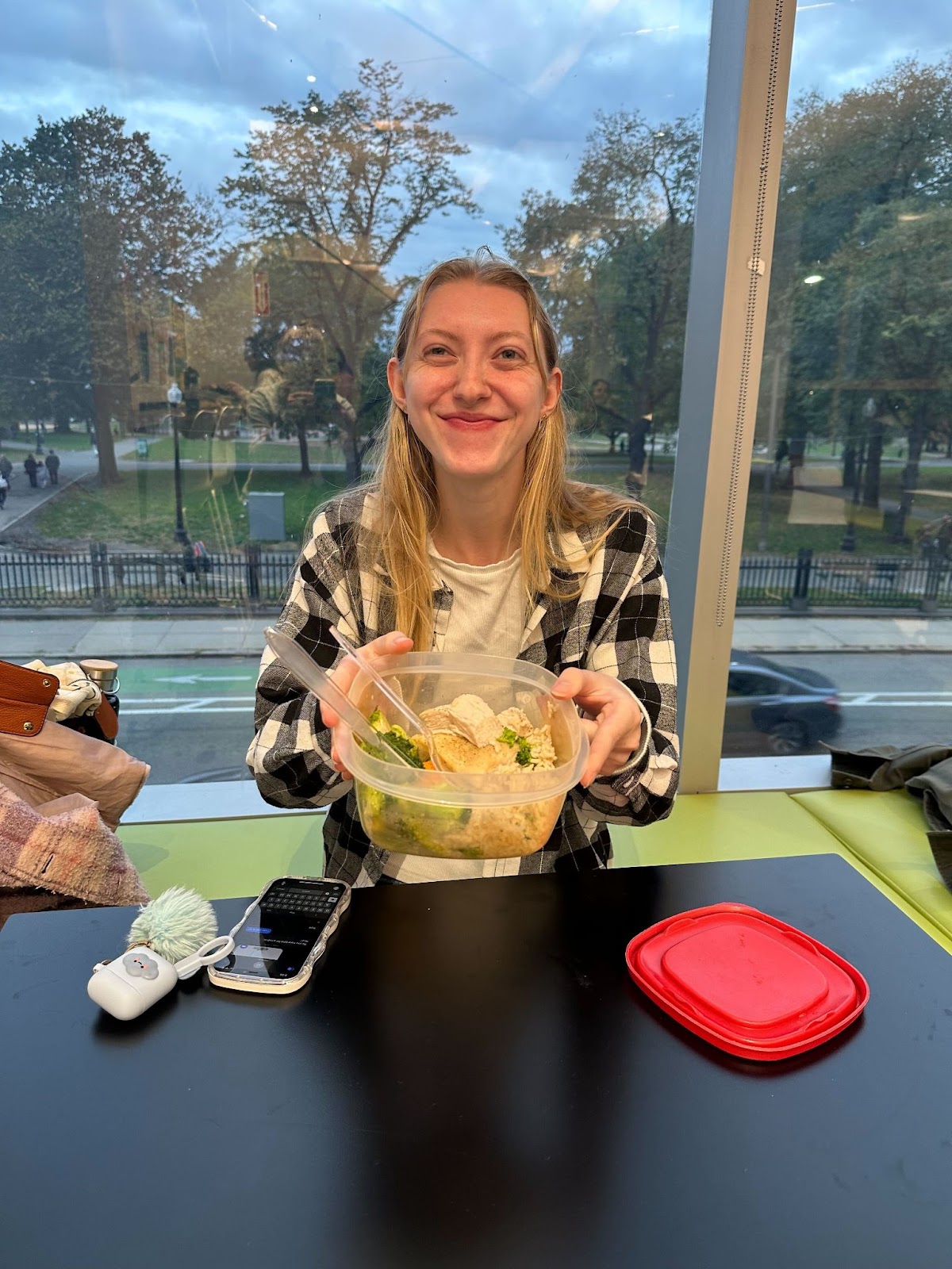 A female student holds up her meal prepped salad with a smile on her face.