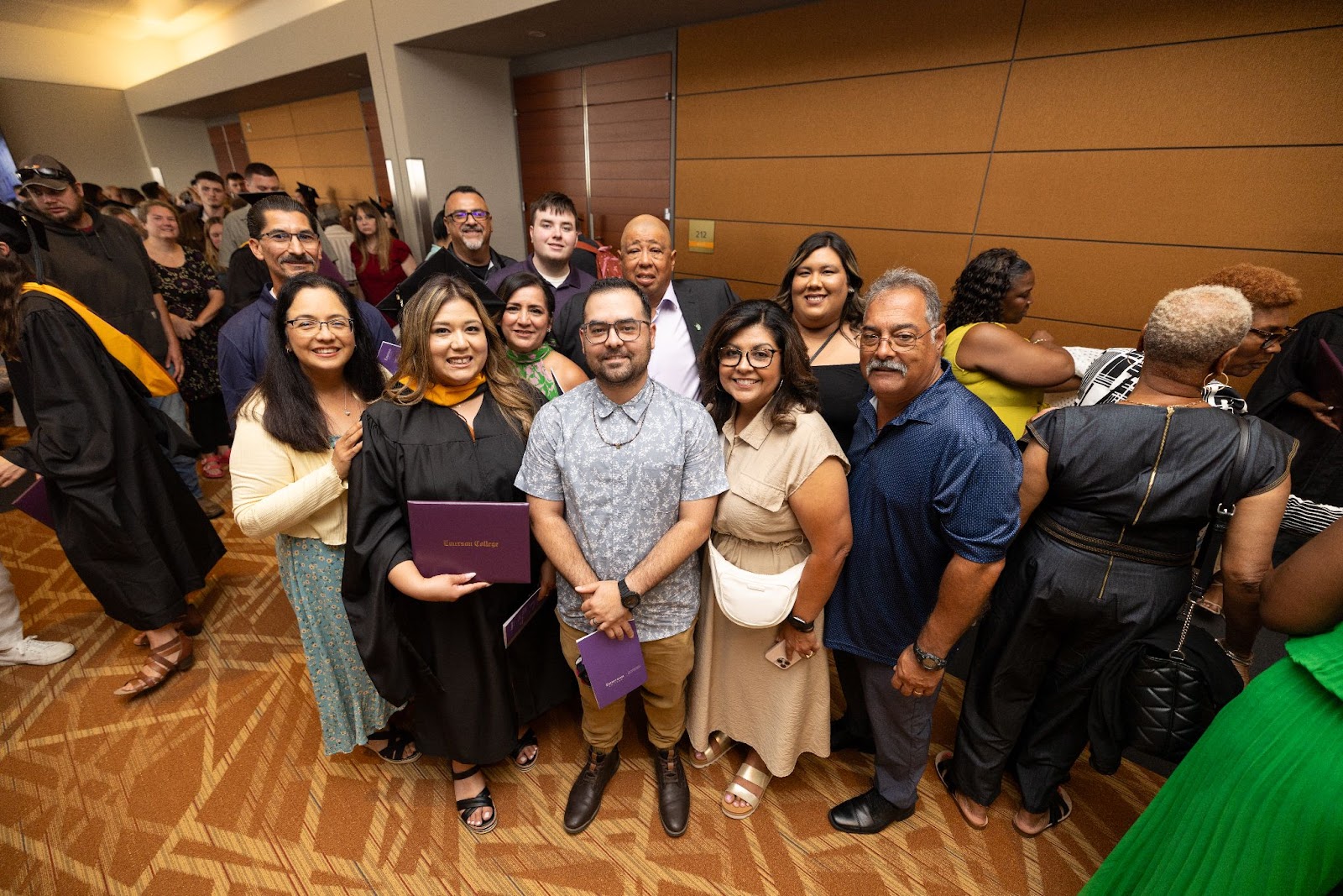 Family smiles up at a camera in the crowded hallway after the hooding ceremony.