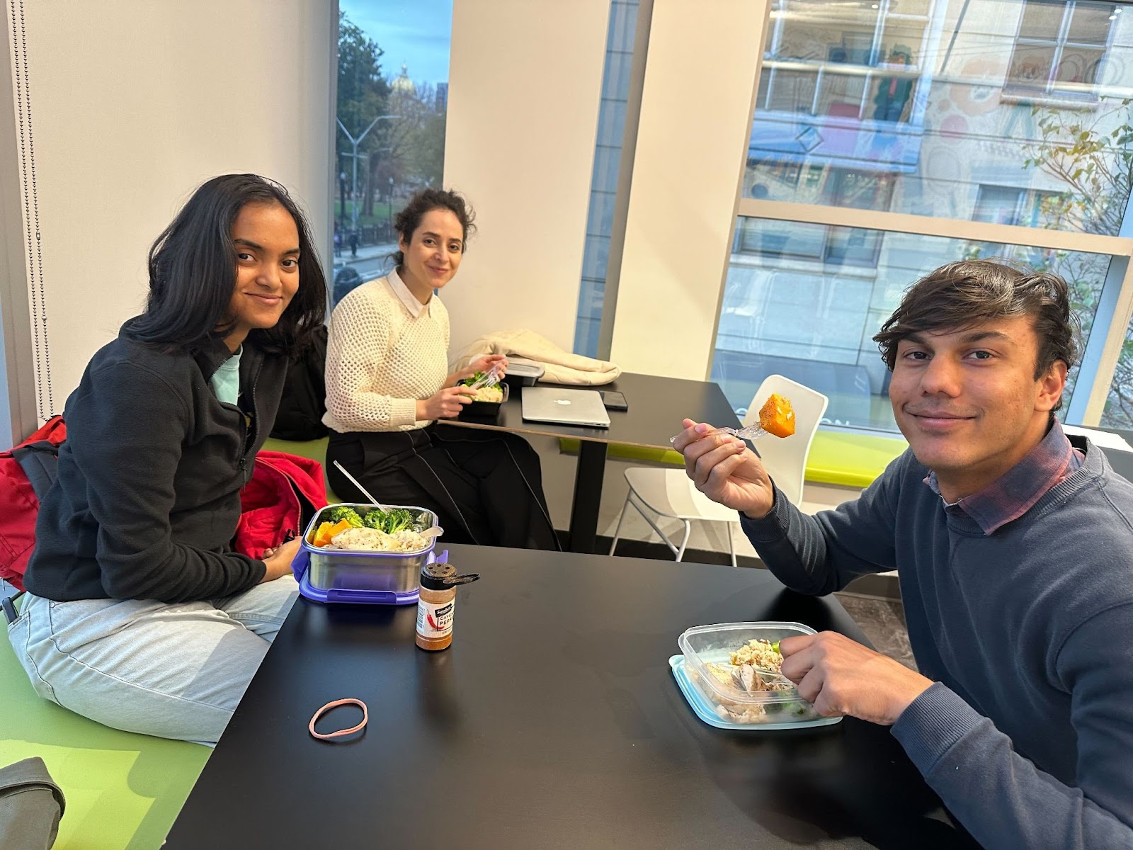 Two students and one professor eat their meals together between two tables.