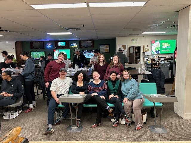 Eight graduate students smile at the camera in an arranged photo at the bowling alley.